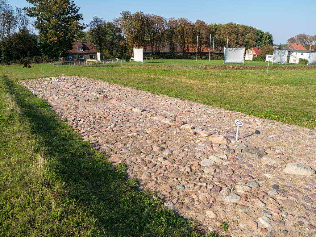 Zweispurige Straße aus Feldstein (Kopfsteinpflaster). Im Hintergrund der Standort der ehemaligen Burg.