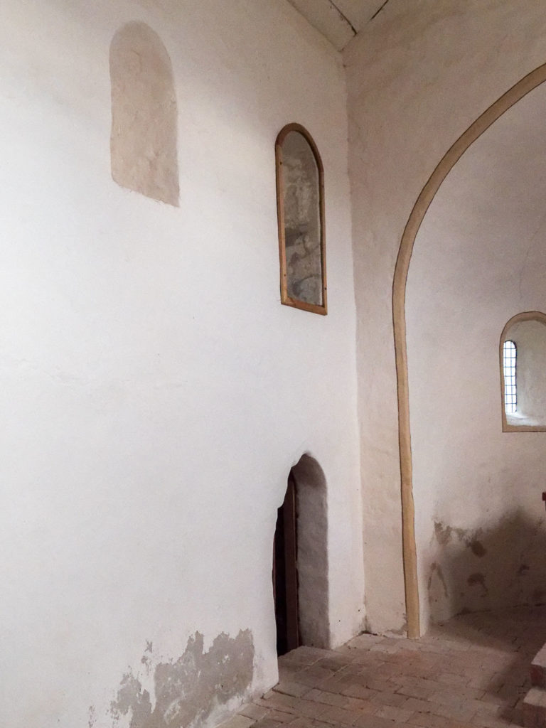 Nordwand des Chors mit zwei romanischen Fenstern zur Sakristei und einer neuzeitlich eingebrochenen Pforte.